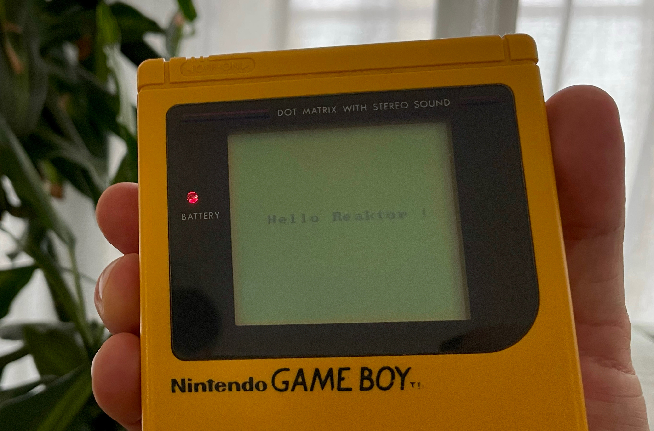 A photo of a yellow Game Boy displaying the text 'Hello Reaktor !'